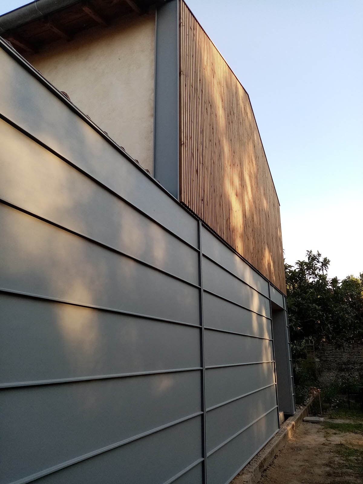 Raccord entre le bardage vertical en bois et l’habillage gris de la façade